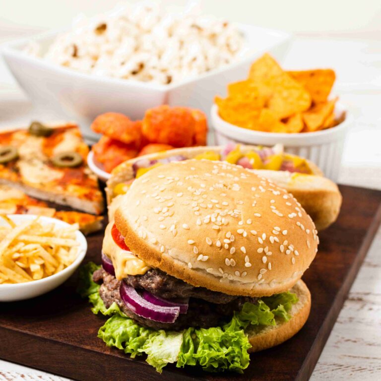 Why We Crave Unhealthy Food: The Biology of Junk Food Cravings Tray with a hamburger, surrounded by hotdog, nachos, rice, pizza, and chicken nuggets.