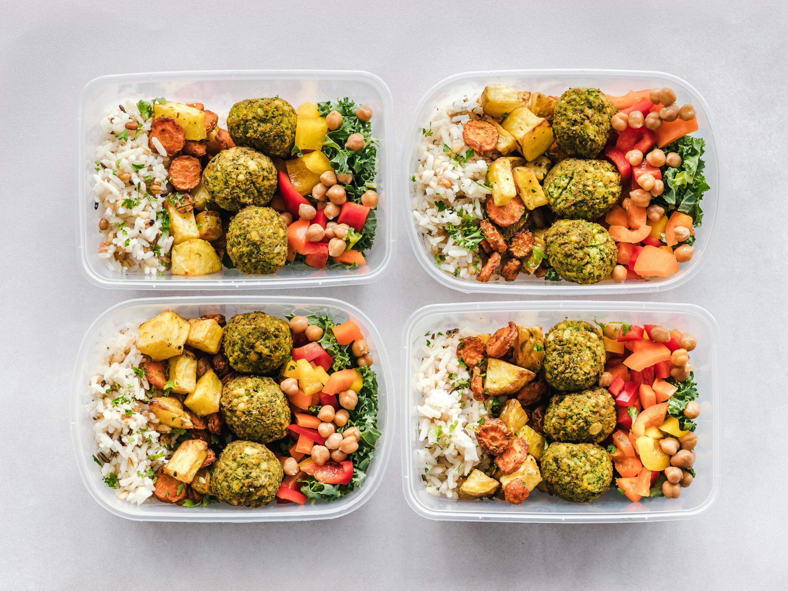 Four food containers with rice, meatballs, potatoes and vegetables